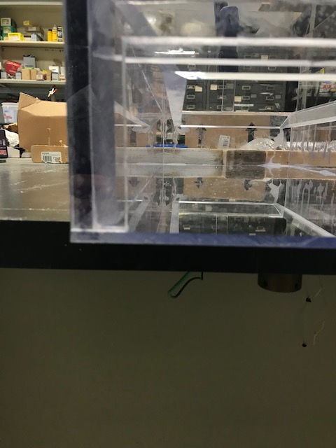 A low-angle view of a transparent, multi-level acrylic structure on a desk in a laboratory or classroom setting.