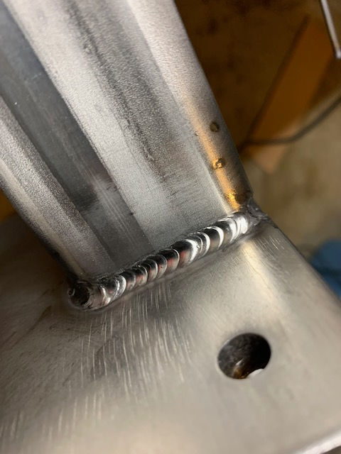 Close-up of a clean TIG weld joining a metal structural beam to a flat plate.