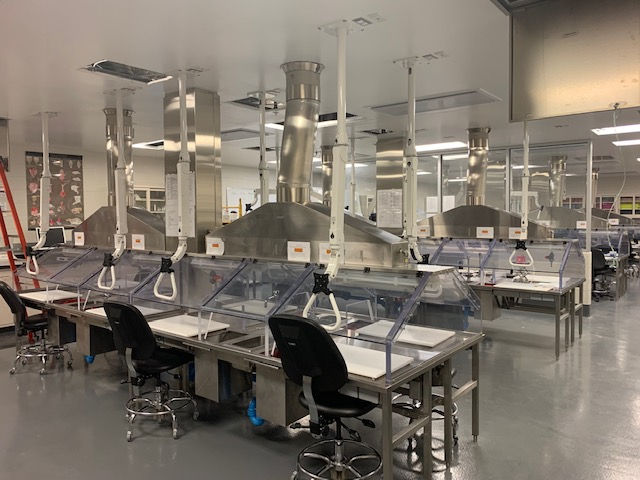 A sterile laboratory featuring rows of individual workstations with ventilation hoods, chairs, and specialized equipment.
