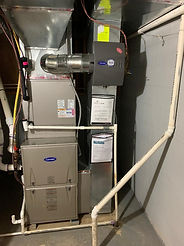 A gray Carrier furnace and central air unit installed in a basement, with connected metal ductwork and white PVC piping.