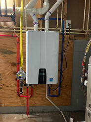 A white tankless water heater mounted on a wooden board, connected to PVC pipes and a yellow gas line in a basement.