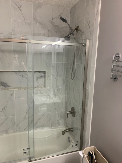 A shower and bathtub combination with marble-patterned tile, a sliding glass door, and chrome fixtures.