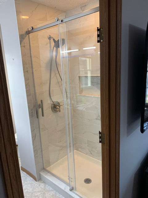 A modern walk-in shower with light marble-style tiled walls, a glass sliding door, and a handheld chrome shower head.