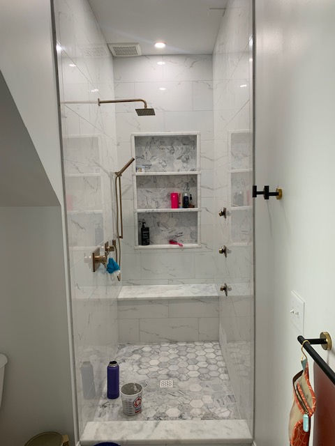 A modern walk-in shower with white marble-look tiles, a built-in bench, gold fixtures, and a recessed three-tier niche.