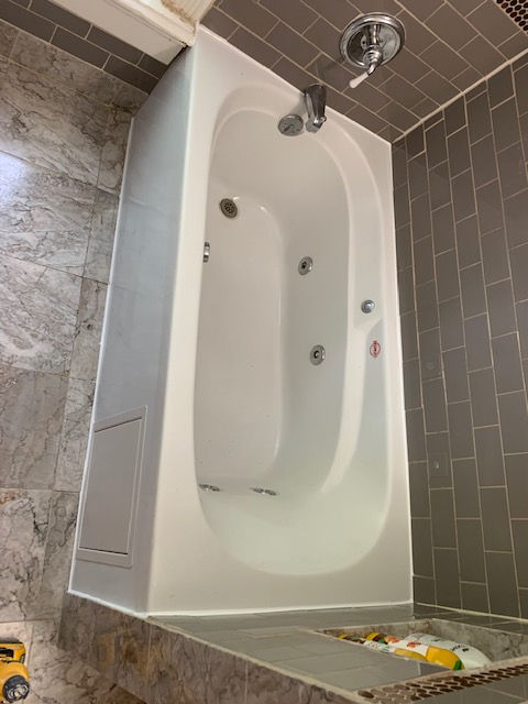 A white whirlpool bathtub with chrome fixtures, set against brown tiled walls and a marble-patterned floor.