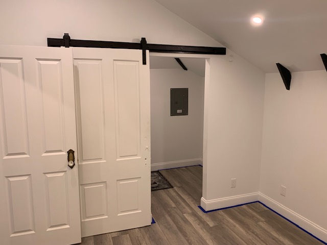 White barn-style sliding doors on a black rail, opening into a small room with wood-look flooring and an electrical panel.
