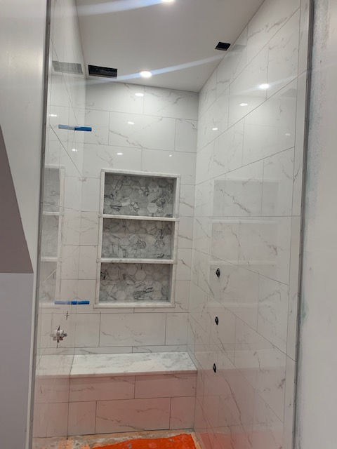 Modern walk-in shower with white marble-look tiles, a built-in bench, and a recessed three-tier shelving niche.