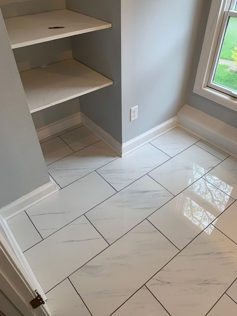 White marble-patterned floor tiles installed in an alcove with two built-in shelves and a window.