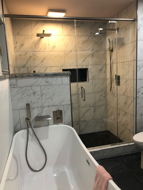A modern bathroom featuring a white soaking tub with a handheld shower head next to a glass-enclosed walk-in marble shower.
