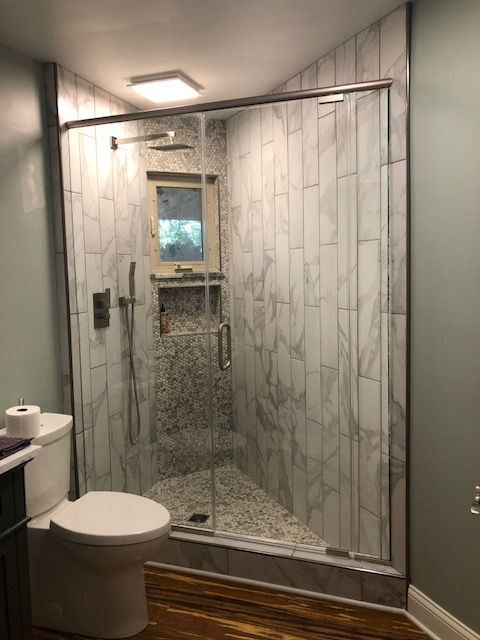 A modern walk-in shower with white marble-style vertical tiles, a built-in corner seat, a glass door, and a toilet nearby.