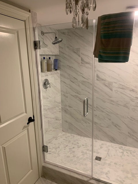 A glass-enclosed shower with white marble-patterned tile, a rainfall showerhead, a built-in niche, and a hanging towel.