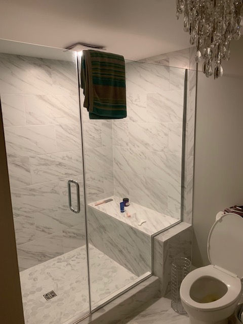 A walk-in shower with white marble tile, a built-in bench, and a glass door, situated next to a toilet in a bathroom.
