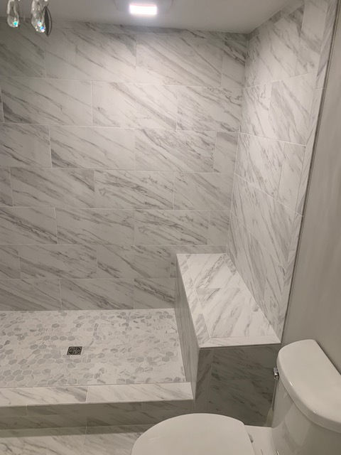 A walk-in shower with a marble tile bench and walls, adjacent to a toilet in a modern bathroom.