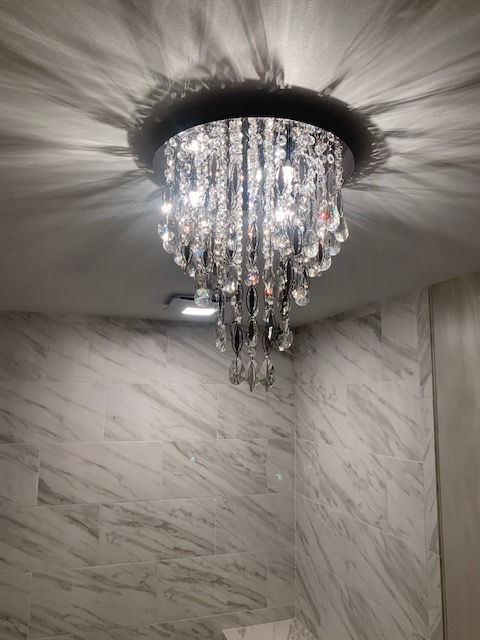 A crystal tiered chandelier glows against a ceiling, casting light onto white marble-patterned walls.