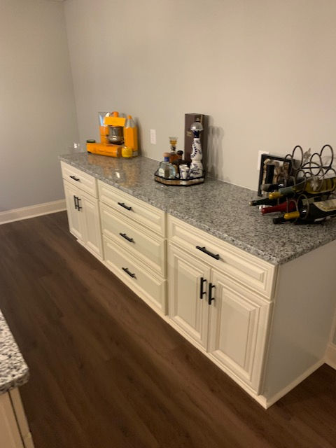 Off-white cabinetry with a granite countertop, holding a coffee machine, a liquor decanter, and a metal wine rack.