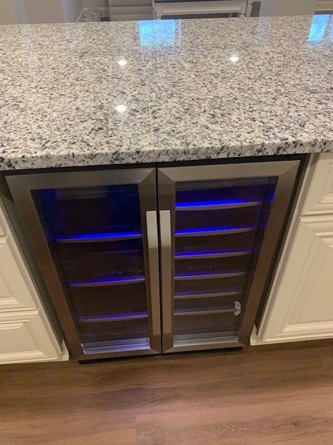 A dual-zone stainless steel wine refrigerator built into a kitchen island with granite countertops and white cabinets.