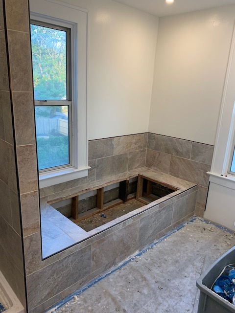 A bathroom renovation showing a tiled, wood-framed bathtub deck under a window.