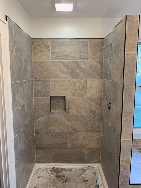 A tiled shower stall with earthy, brown-toned rectangular tiles and a built-in recessed niche on the back wall.