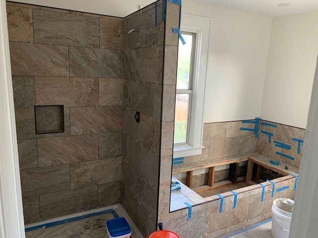 A bathroom undergoing renovation features a tiled shower stall and a bathtub surround with exposed wooden framing.