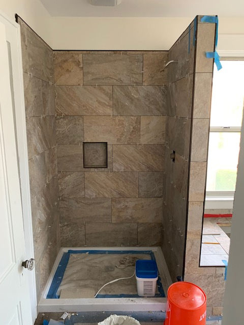 A bathroom shower under construction with earth-toned, rectangular wall tiles and a white shower pan floor.