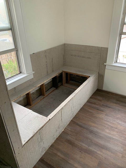 A partially constructed L-shaped bench seat framed with wood and covered in cement board in a room with wood-look flooring.
