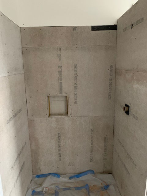 A tiled shower enclosure under construction with gray cement board walls and a recessed soap niche.