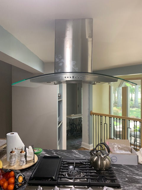 A stainless steel kitchen island range hood with a glass canopy, positioned above a stovetop in a home kitchen.