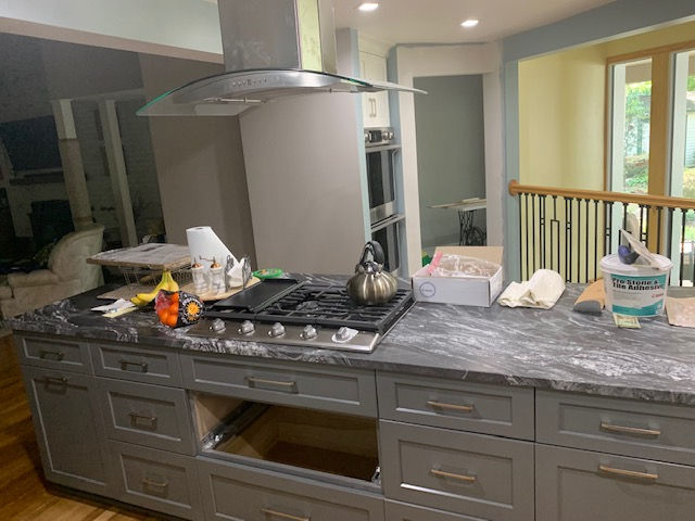 A kitchen island with a dark stone countertop, a gas cooktop, and gray cabinets, featuring an empty oven space.