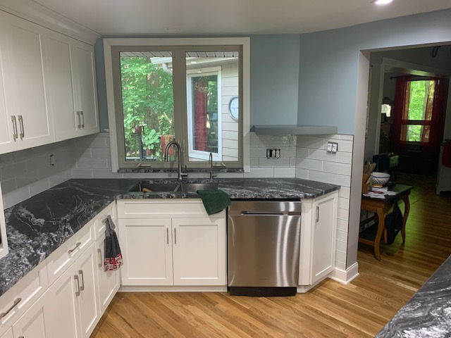 A modern kitchen with white cabinets, dark gray granite countertops, a stainless steel dishwasher, and a window over a sink.