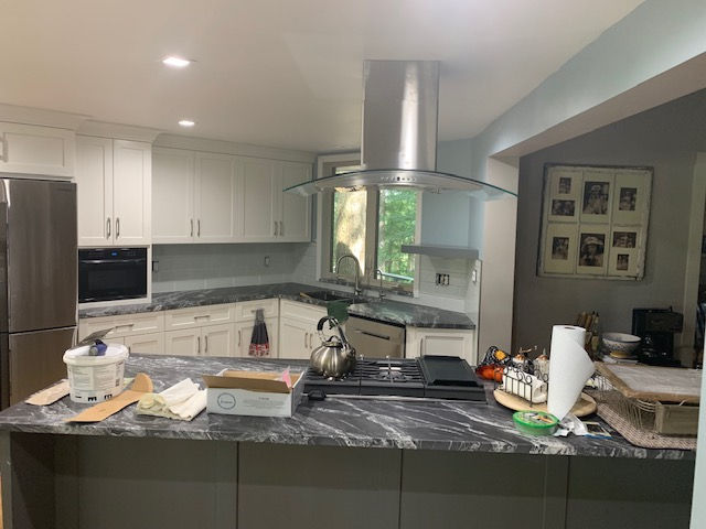 Modern kitchen with white cabinets, dark marble countertops, a central island, and a stainless steel vent hood.