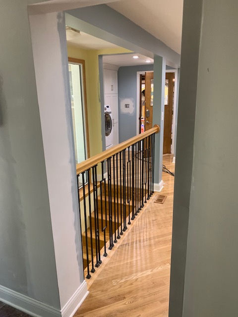 An interior view looking down a wooden staircase with black metal balusters and a light wood railing through a doorway.