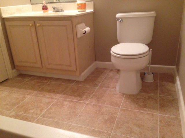 A beige bathroom vanity next to a white toilet with a toilet brush, set against beige walls and tiled flooring.