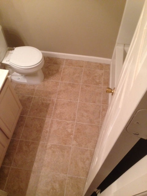 A top-down view of a small bathroom featuring tan square tiled floors, a white toilet, and a white vanity cabinet.