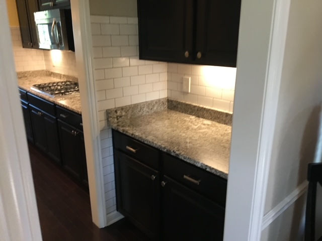 A kitchen with dark cabinets, granite countertops, and white subway tile backsplash, viewed through a doorway.