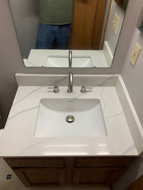 A vanity with a white, marble-patterned countertop, a rectangular sink, a silver faucet, and a mirror in a bathroom.