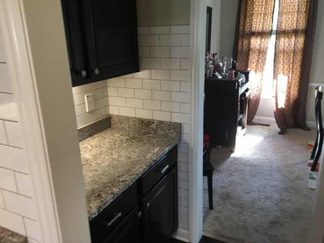 A small kitchen area with dark cabinets, a stone-patterned countertop, and white subway tile backsplash.