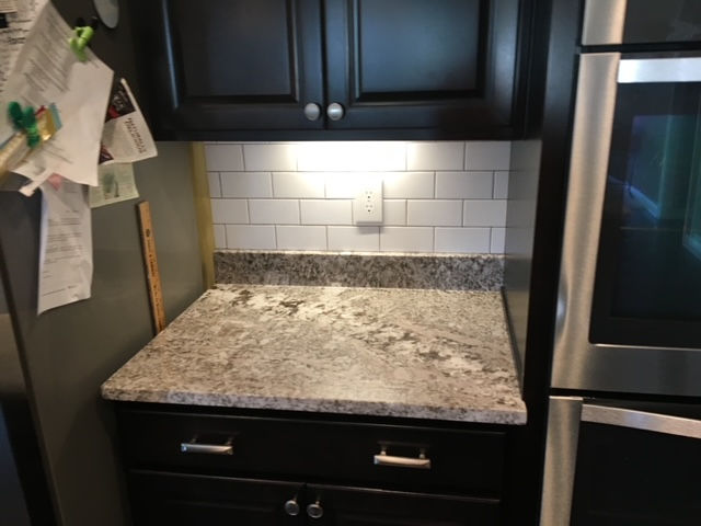 A kitchen countertop with granite, white subway tile backsplash, and dark wood cabinets next to a stainless steel oven.