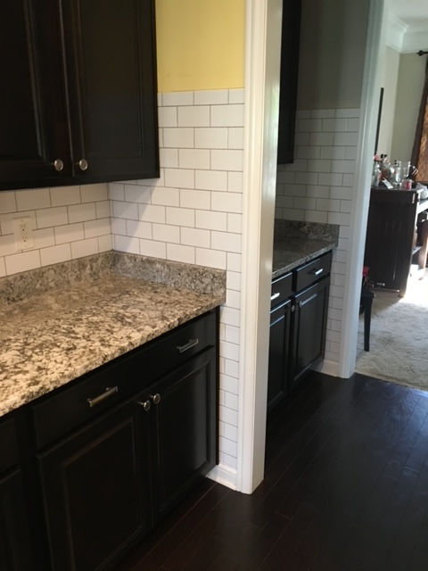 Dark wood kitchen cabinets with granite countertops and white subway tile backsplash viewed from a doorway.