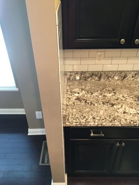 A kitchen counter with mottled granite, white subway tile backsplash, and dark brown cabinets next to a beige wall corner.
