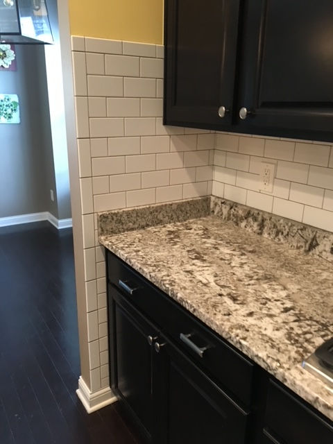 A kitchen counter with granite top, white subway tile backsplash, and dark brown cabinets extending to a wall edge.