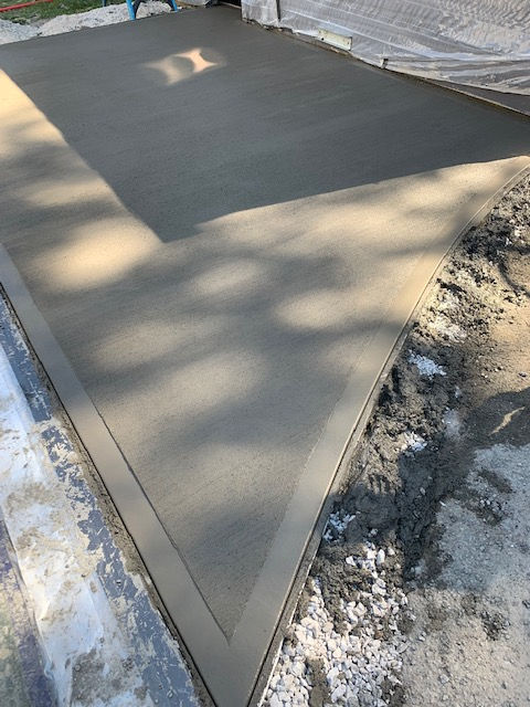 Freshly poured gray concrete driveway with a smooth border, surrounded by unfinished dirt and debris.