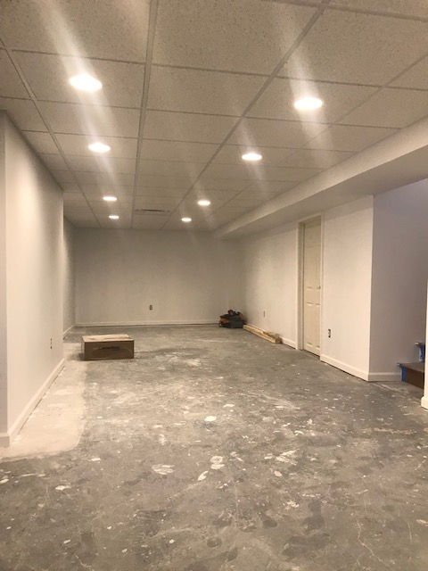 A basement room with white walls, a drop ceiling with recessed lighting, and an unfinished concrete floor.