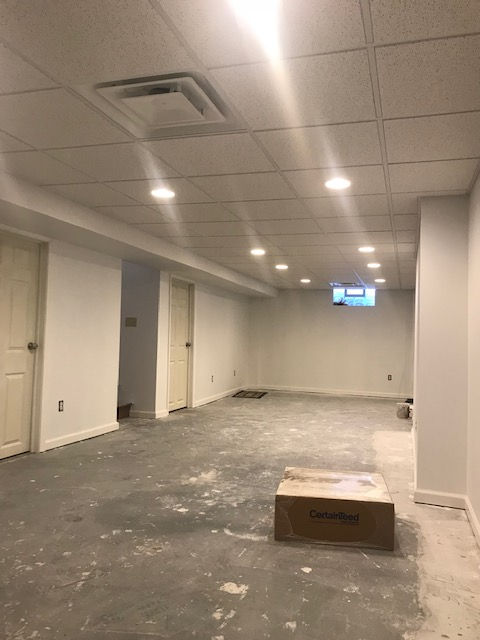 An unfinished basement room with white walls, a drop ceiling with recessed lights, and a concrete floor.