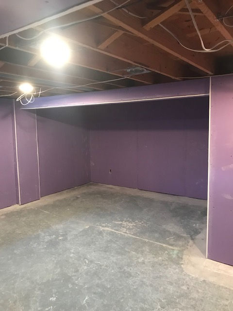 An unfinished basement room with purple drywall, an exposed wooden ceiling, and a concrete floor.