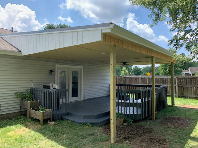 A backyard deck featuring a covered patio, a grey railing, a pair of French doors, and two small wooden planter boxes.