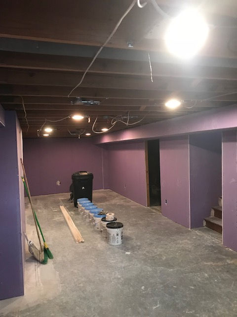 Unfinished basement with purple drywall, exposed ceiling joists, scattered construction tools, and paint buckets.