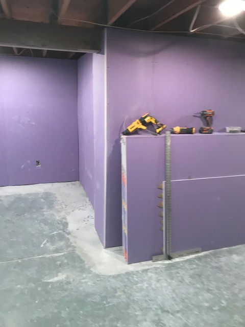 A room under construction with purple drywall installed on the walls and a T-square leaning against a wall partition.