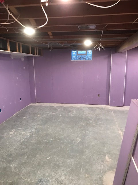 A basement room under renovation with purple drywall on the walls, an exposed ceiling, and a concrete floor.