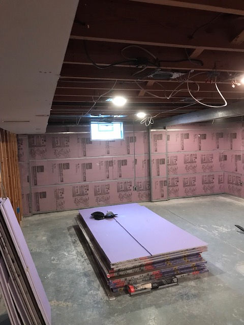 A basement under construction featuring purple foam insulation boards installed on the walls and stacked in the center.