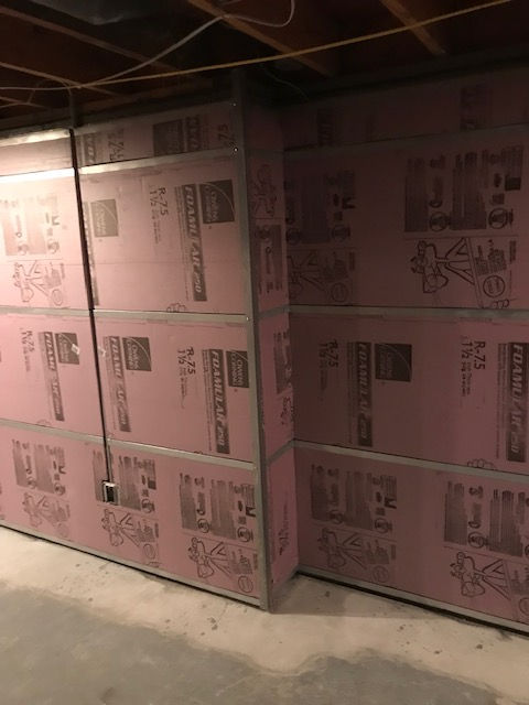 Basement wall partially finished with pink rigid foam insulation boards and metal studs.